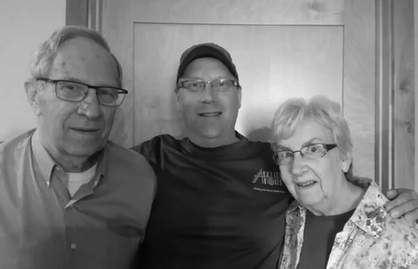 Three people smiling and posing for a photo indoors, with two men and one woman, all wearing glasses.