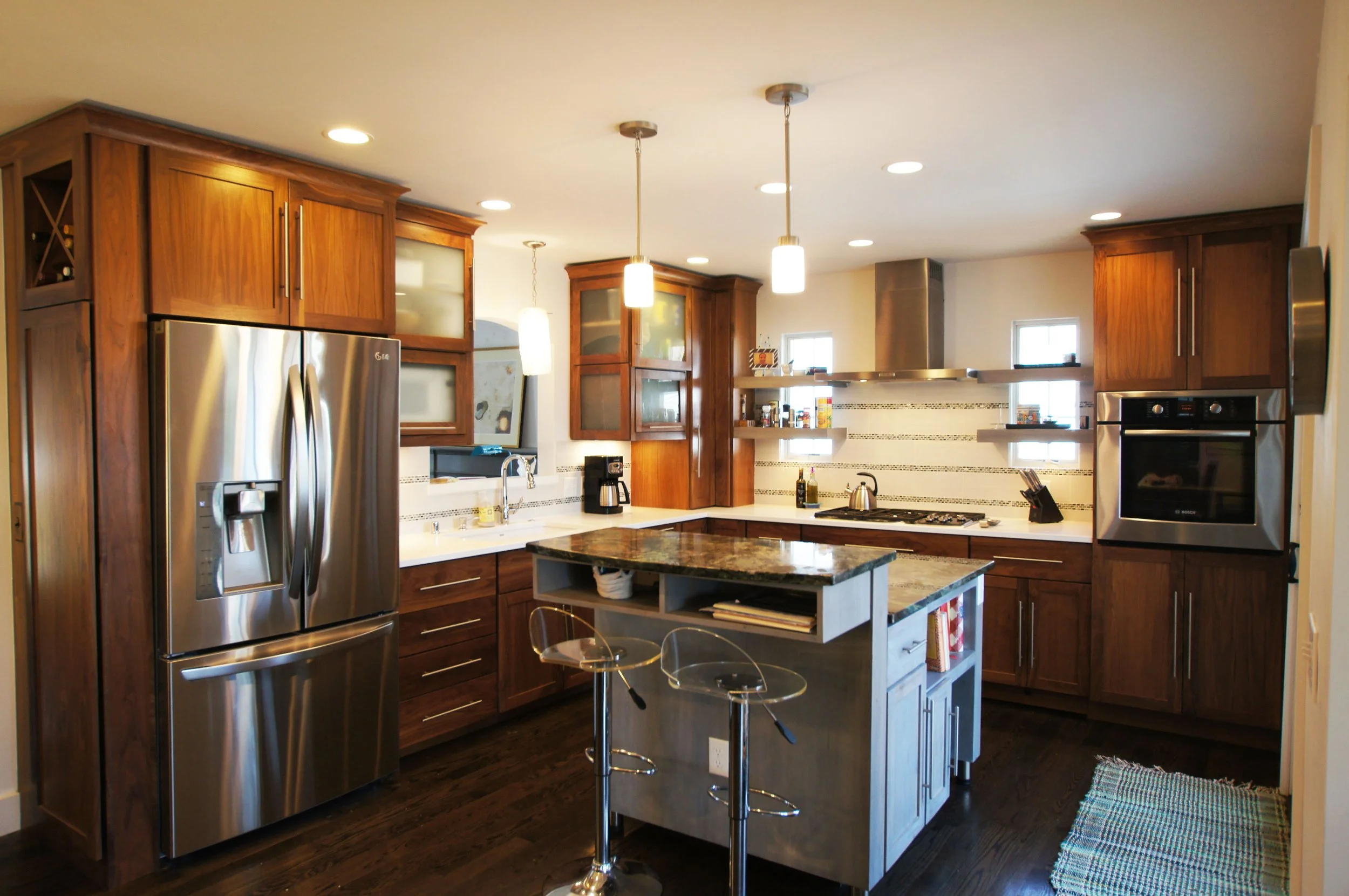 Modern kitchen with wooden cabinets, stainless steel appliances, a central island with a granite countertop, pendant lights, and small windows.