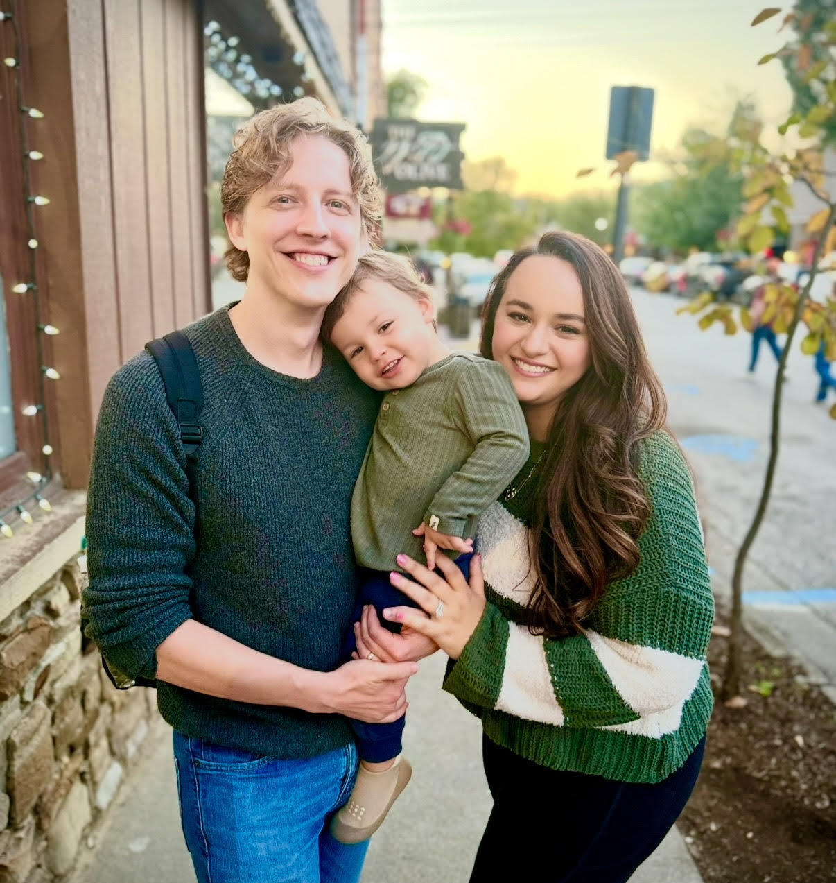 Pediatric dentists Dr. Matt and Dr. Monica and their son smiling on the street in Noblesville, IN. Wearing earth tones.