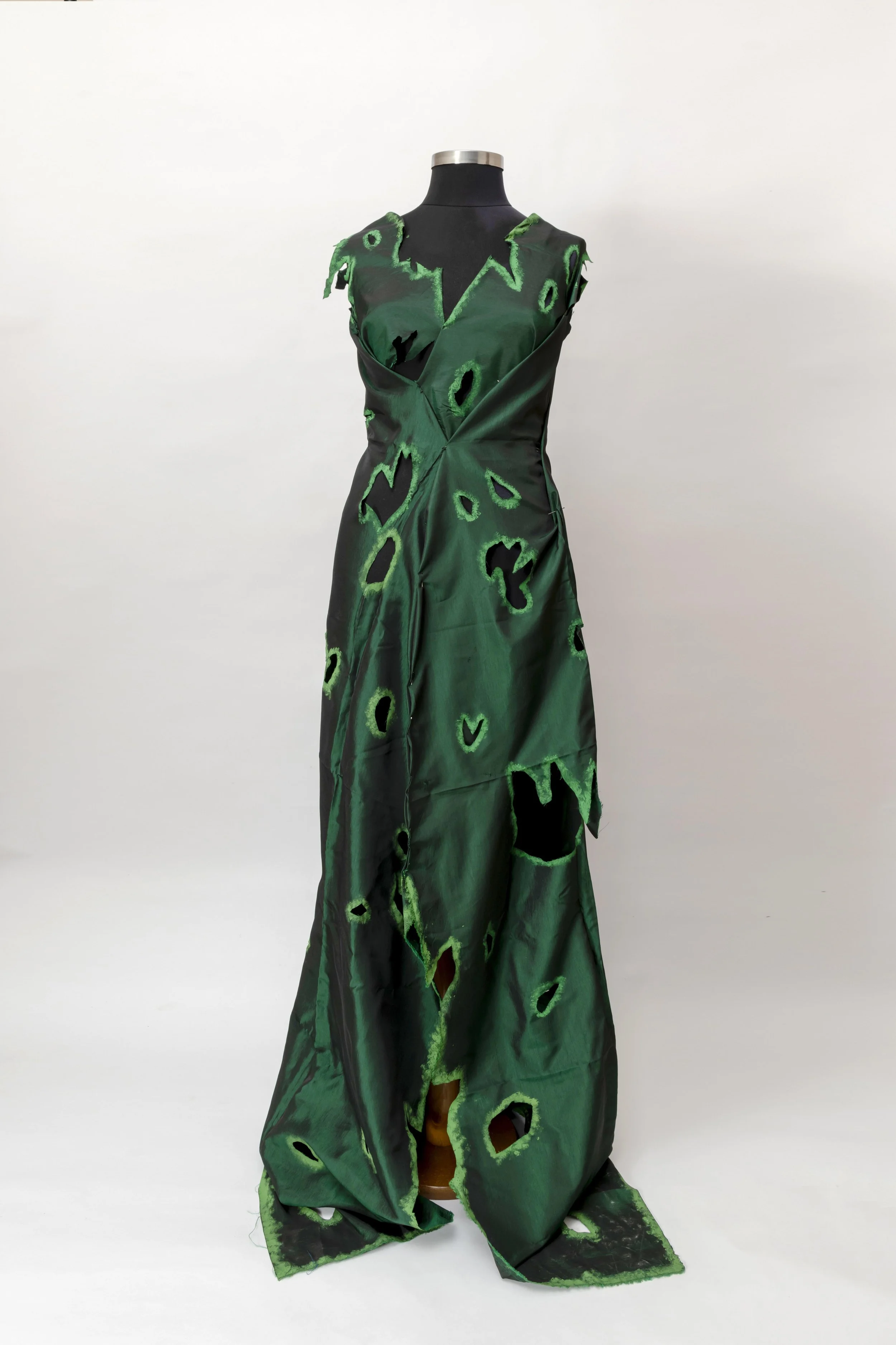 A long dress on a black mannequin with a plain white background. The dress is green with black and cut-out pattern details.LEA BAZIN, DOĞU & ERİNÇ PORTFOLYO HAZIRLIK ATÖLYESİ VE EĞİTİM DANIŞMANLIĞI
