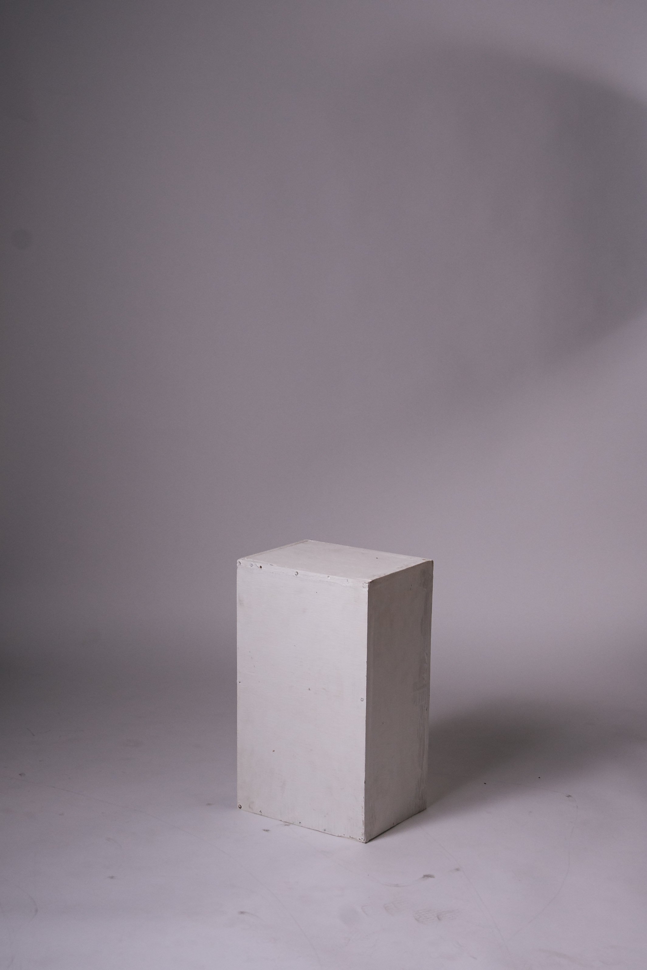 A white rectangular pedestal standing on a light gray surface with a gradient gray background.