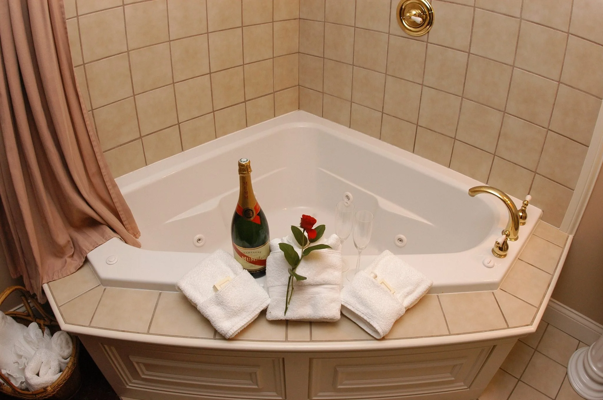 Bathroom bathtub with champagne, a rose, towels, and champagne glasses arranged for a celebration.