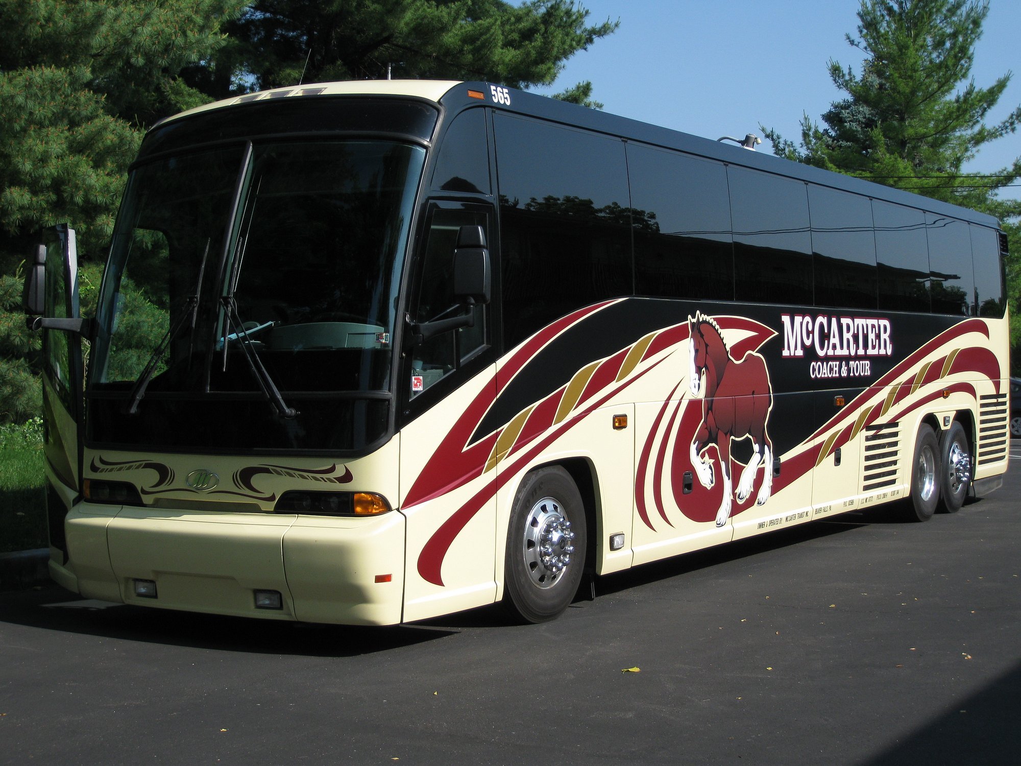 A black and cream coach bus with a large horse graphic and the text "McCarter Coach & Tour" parked on a paved lot, with trees in the background.