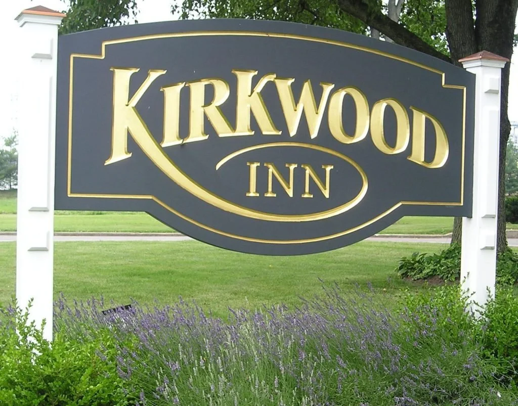 Sign for Kirkwood Inn with gold lettering on a black background, surrounded by greenery and purple flowers.