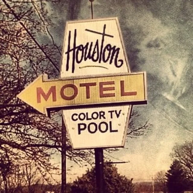 A vintage roadside sign for Houston motel, advertising color TV and pool, with a background of trees and a cloudy sky.