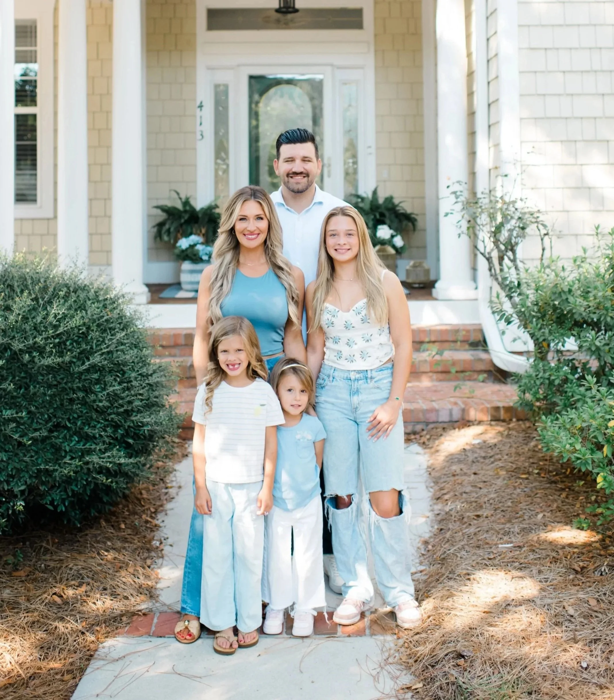 Family of five standing on a sidewalk in front of a house, smiling for a photo.