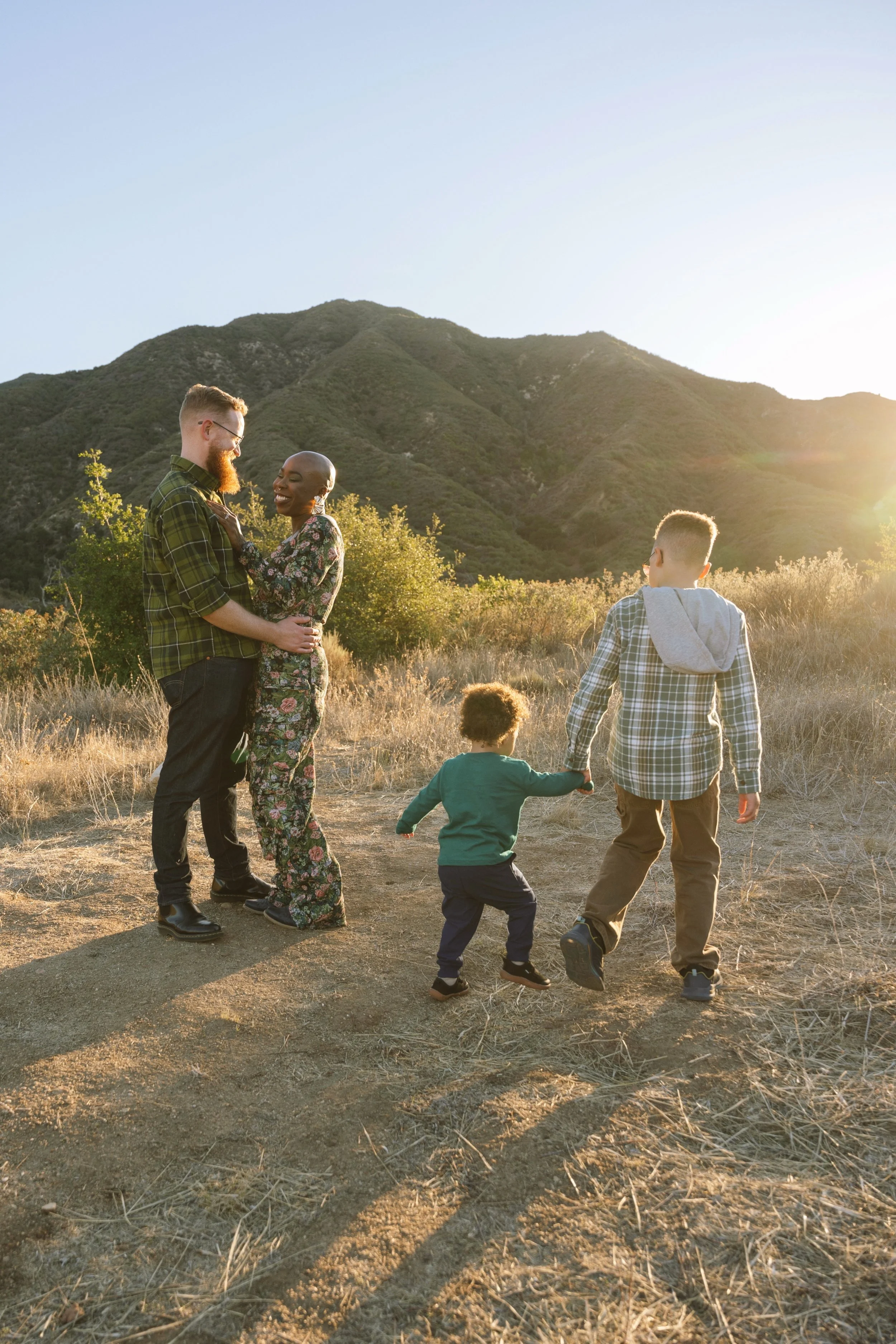 Family enjoying outdoor walk in a mountain meadow at sunset, holding hands and smiling.