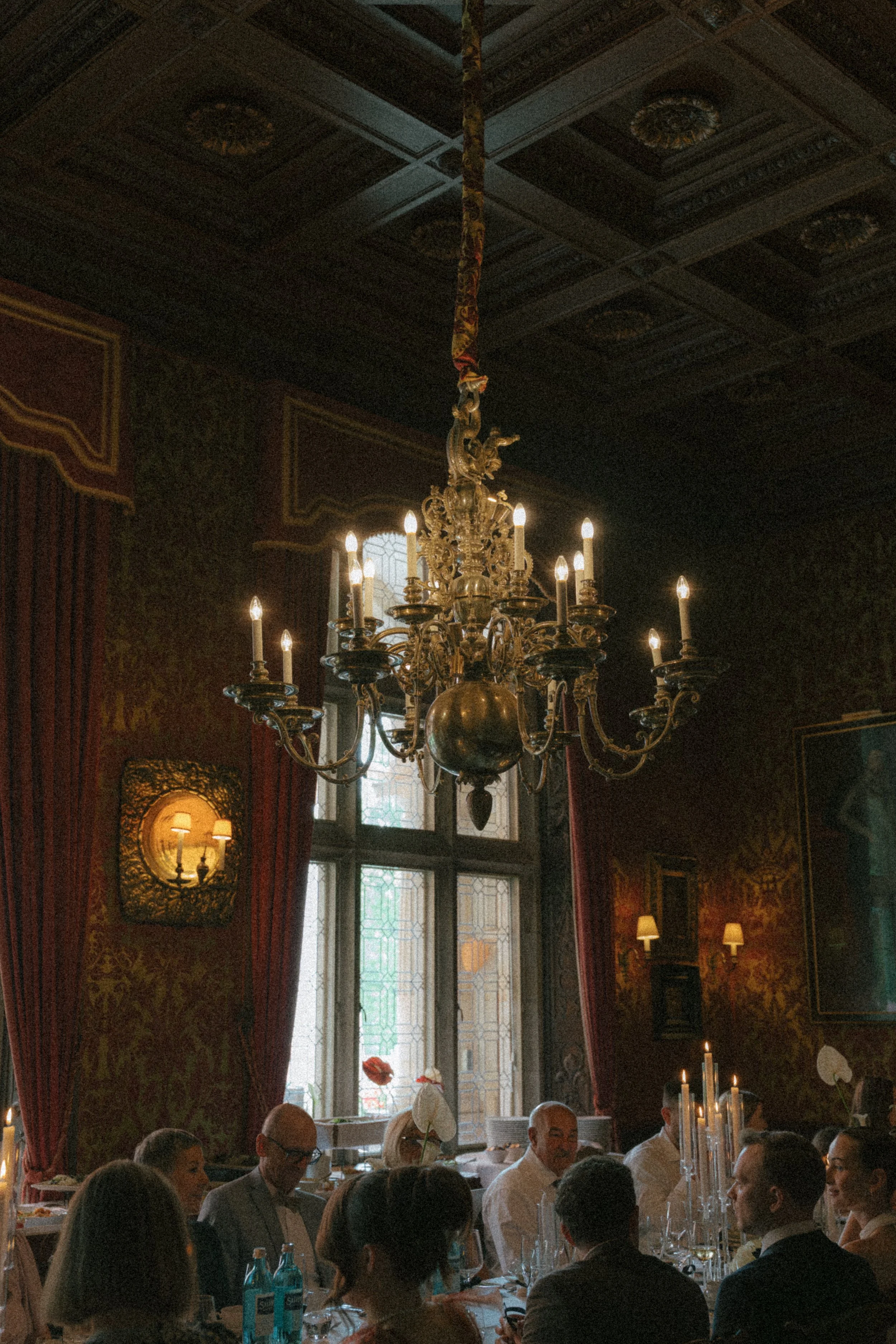 Hochzeitsgesellschaft im Schlosshotel Kronberg sitzt an einer langen tafel, über ihnen ein Kronleuchter. Das Bild ist Vintage angehaucht.