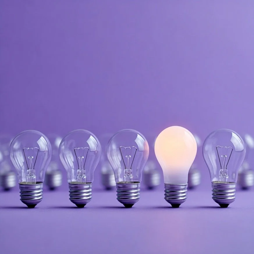 Row of five light bulbs on purple background, with the middle one turned on and glowing.