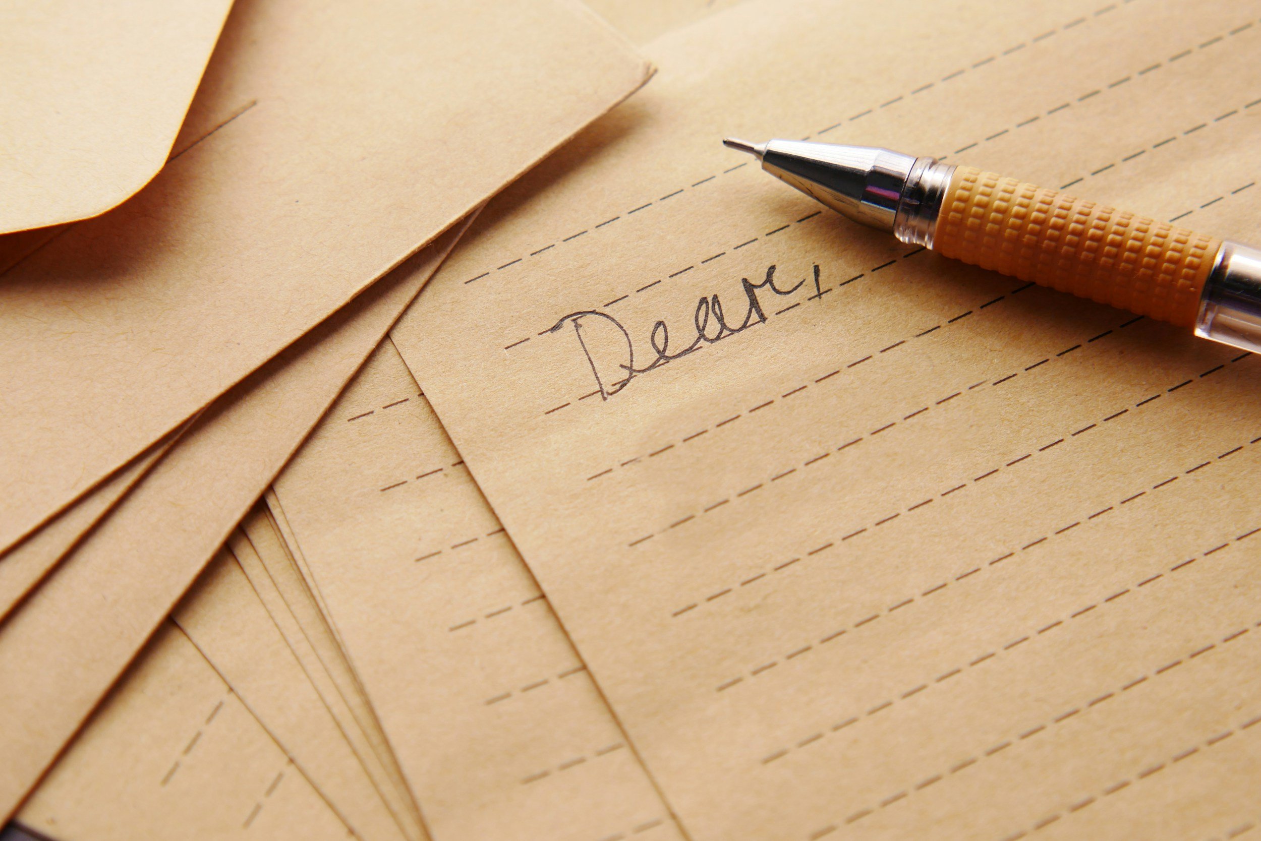 A stack of brown paper sheets, one with the word 'Dream' written in cursive, and a pen resting on top.
