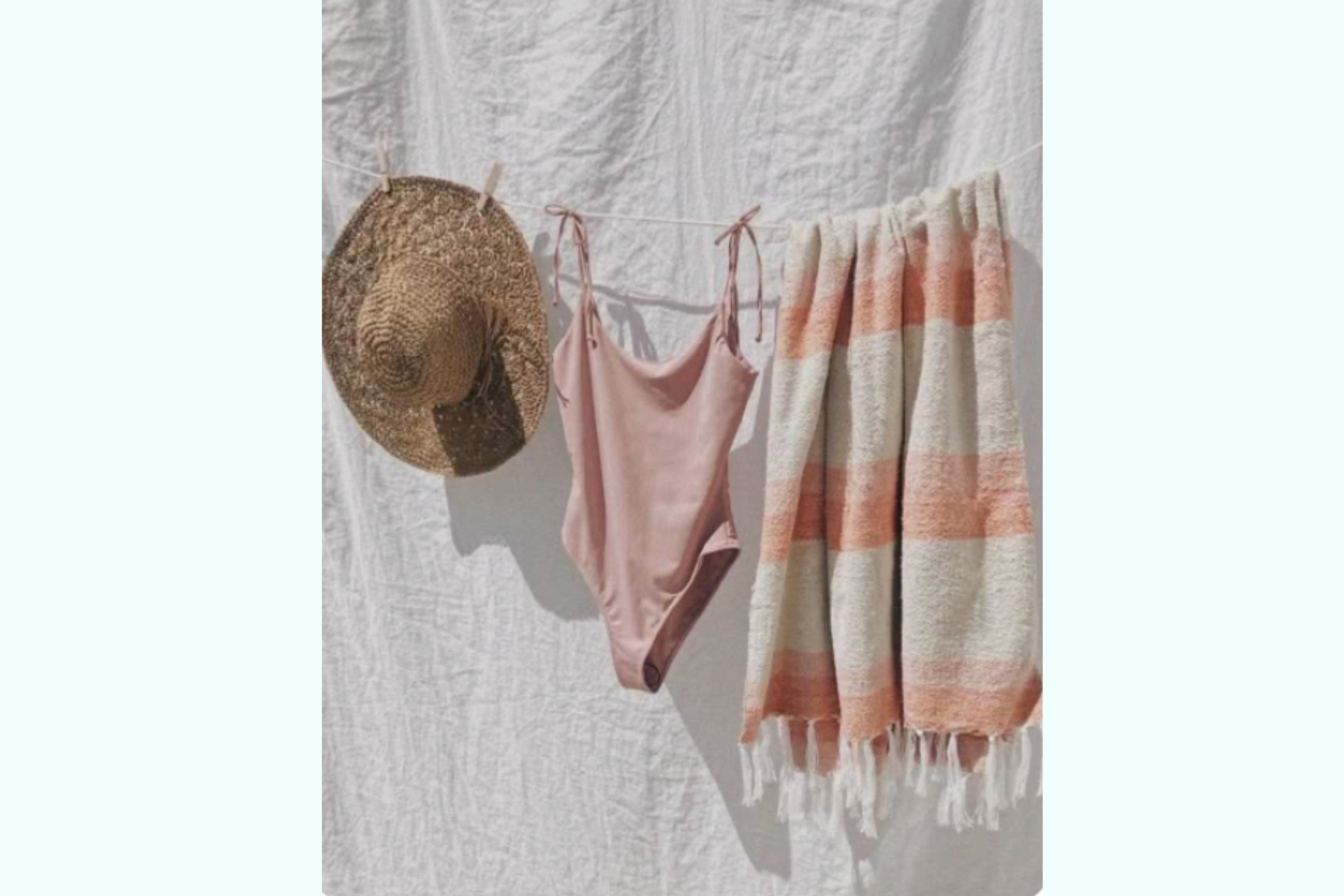 A straw sun hat, pink lingerie, and a striped towel hanging on a clothesline against a white fabric background.