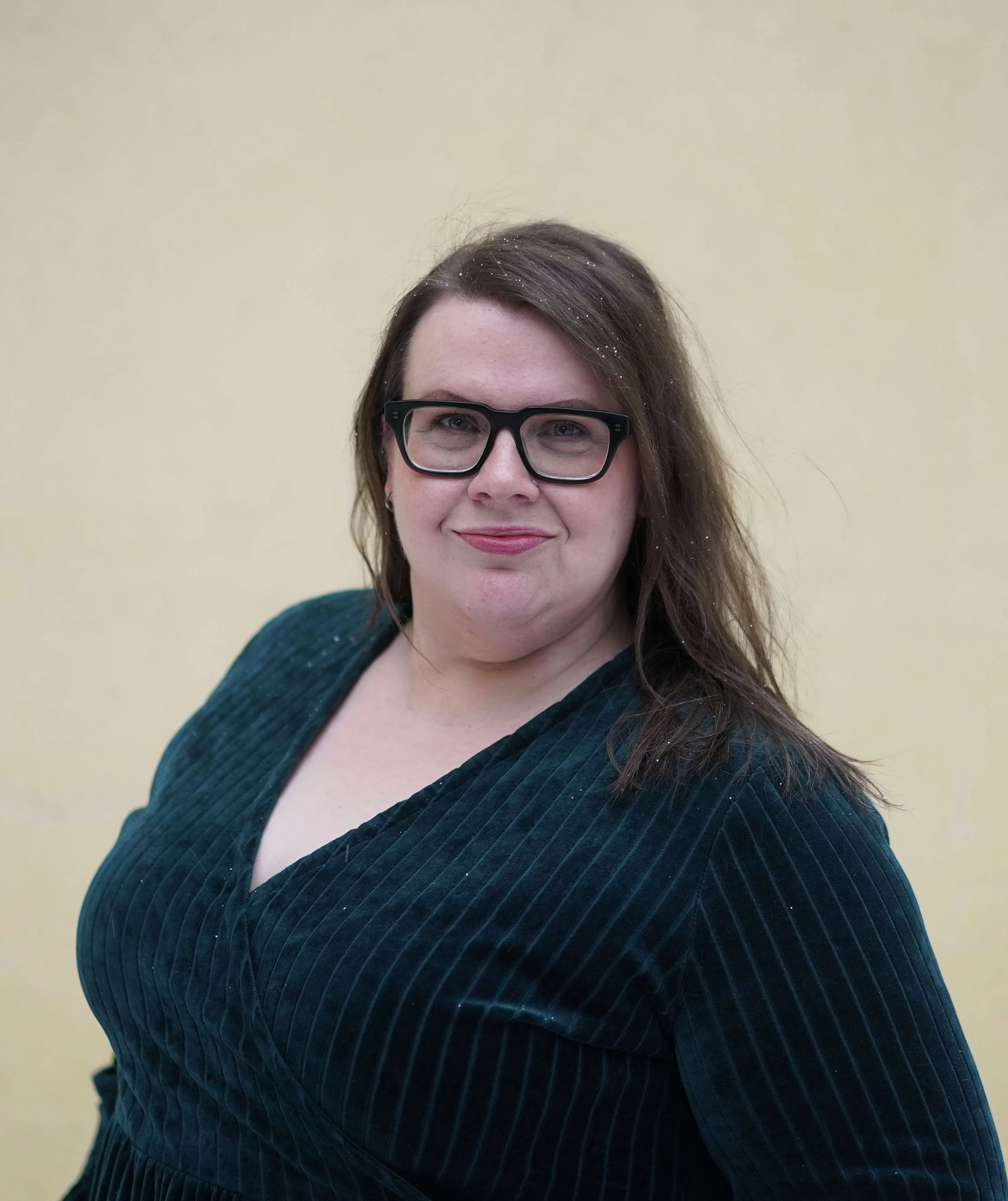 Suvi Eriksson looking straight to the camera photographed outside wearing glasses and a velvet petrol colour dress.