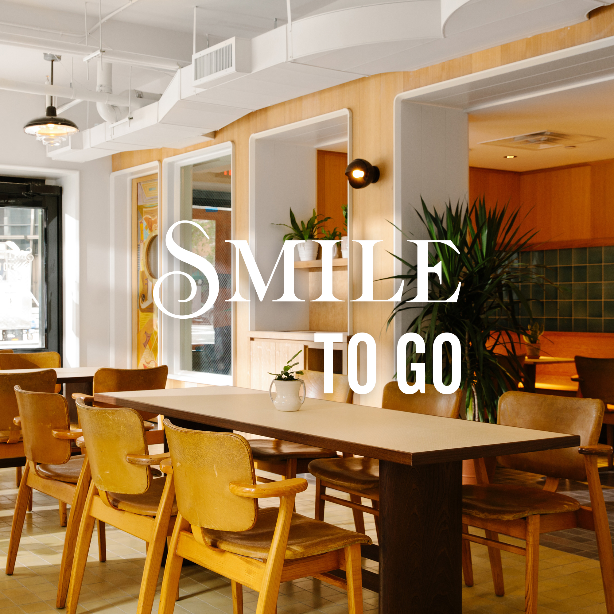 Interior of a modern cafe with wooden chairs and tables, potted plants, and natural light, overlayed with the text 'Smile to Go'.