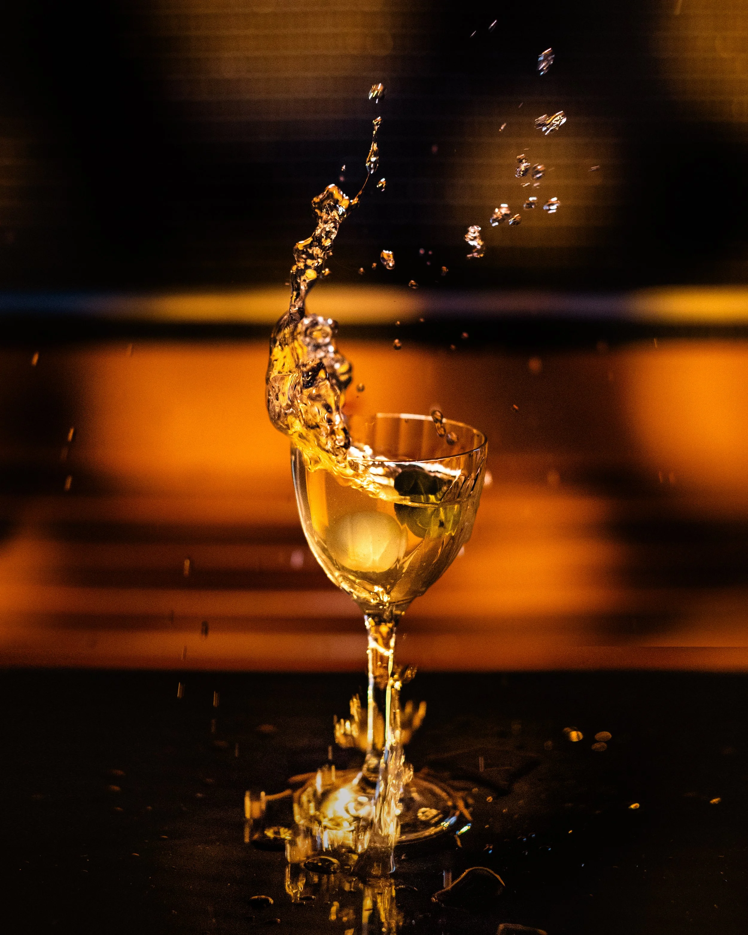 A golden-hued martini glass with a splash mid-air against a dark background with warm lighting.