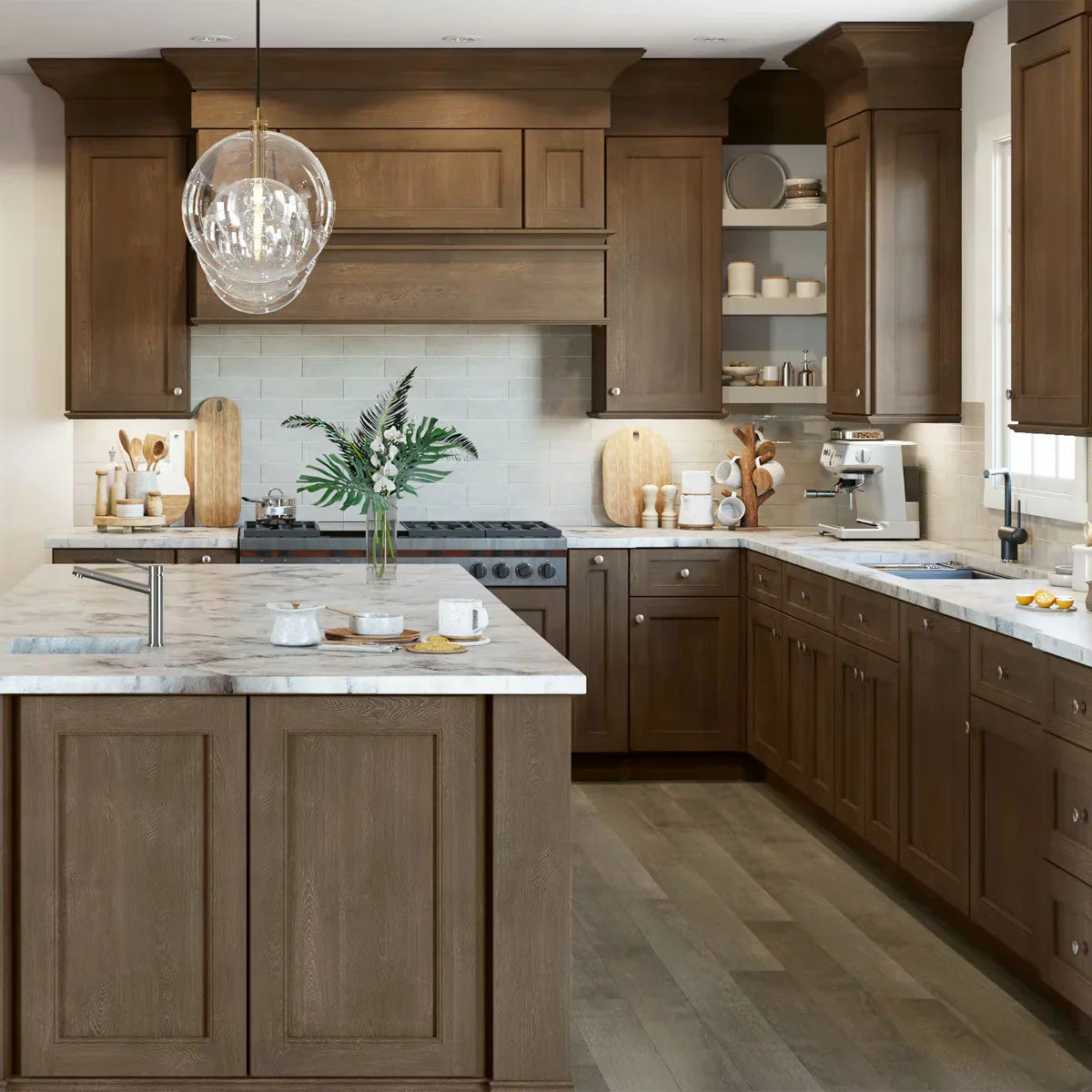 A modern kitchen with wooden cabinets, a marble island, and a white tiled backsplash. Decor includes a vase with green leaves, cutting boards, and baked goods on the counter. Coffee machine and sink are visible.