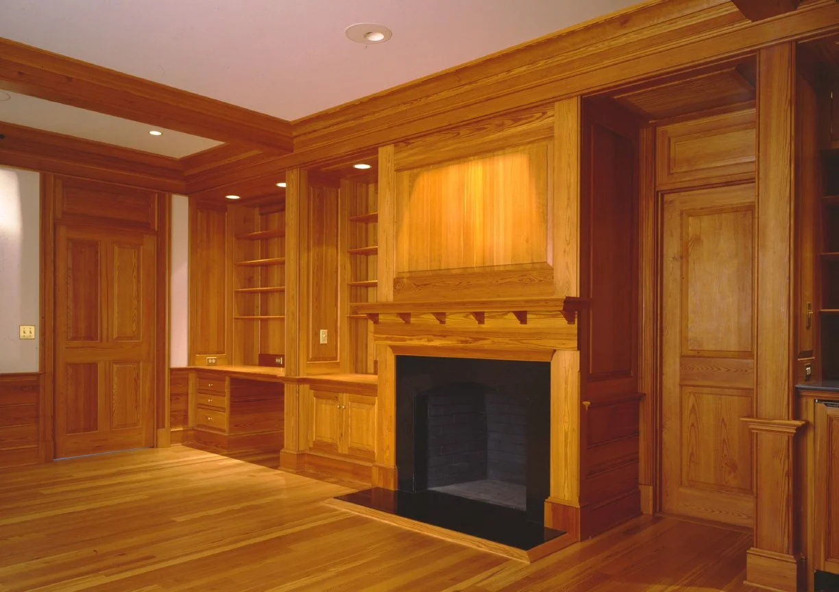 A room with wooden paneling, built-in shelves, and a fireplace with a black interior, wood mantel, and a decorative wooden surround, in a warm-toned interior.