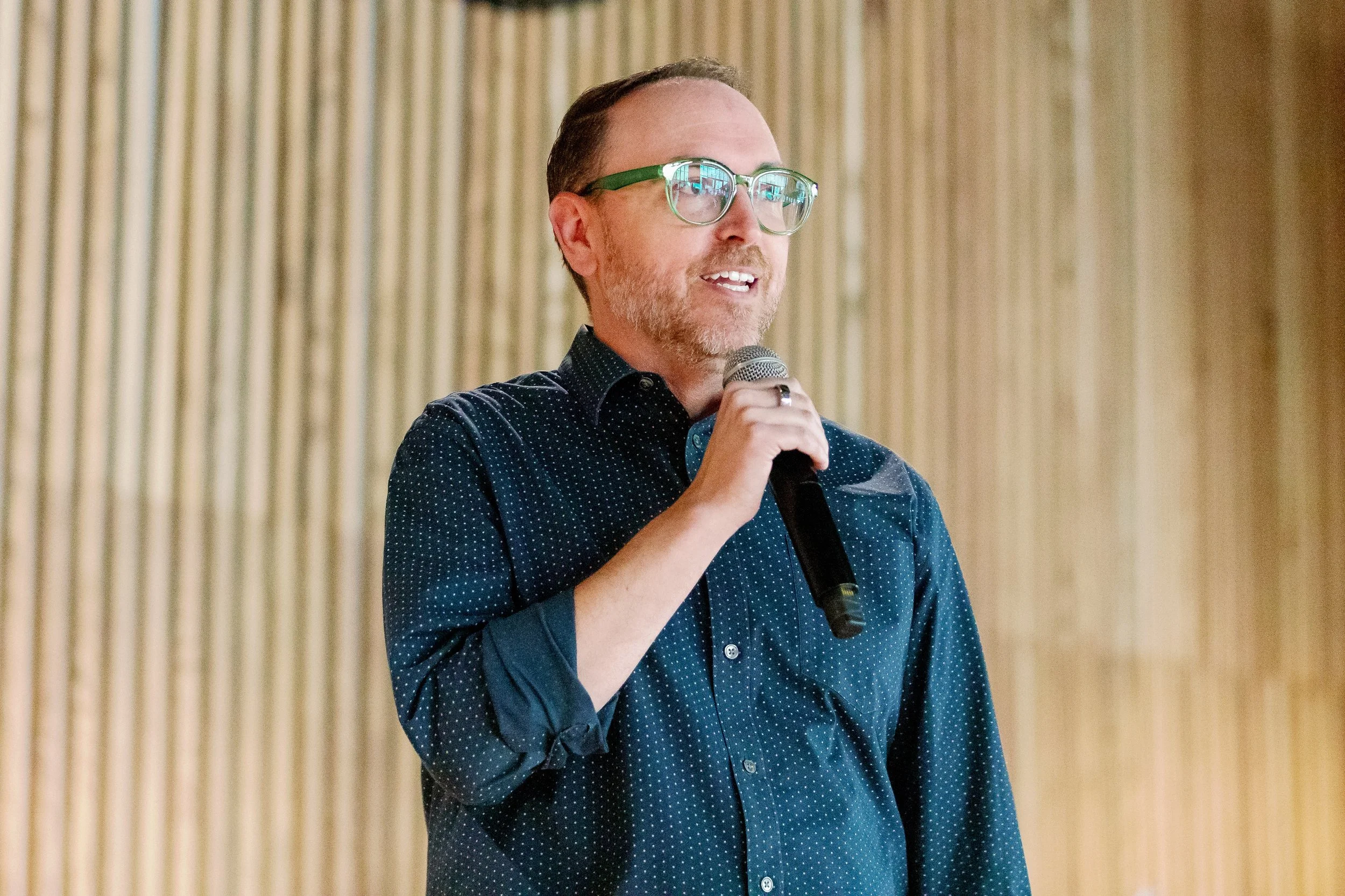 A man with glasses speaking into a microphone at an indoor event.
