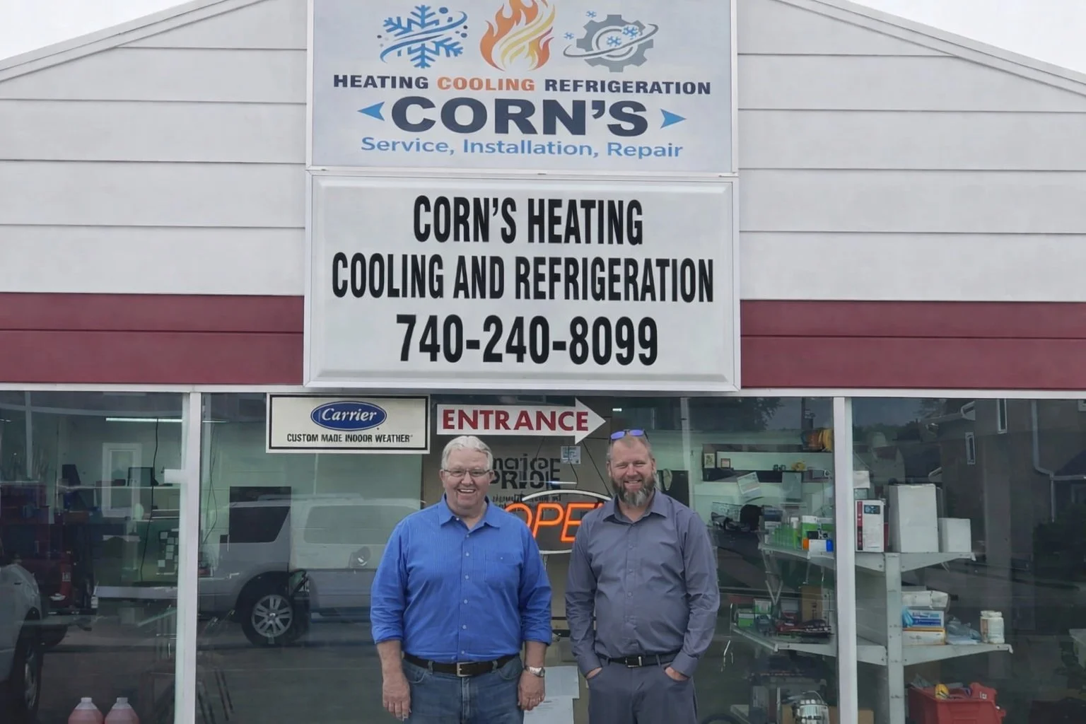 Two men standing outside an HVAC repair shop with a sign for heating, cooling, and refrigeration services. The shop has a glass storefront showing HVAC equipment inside.