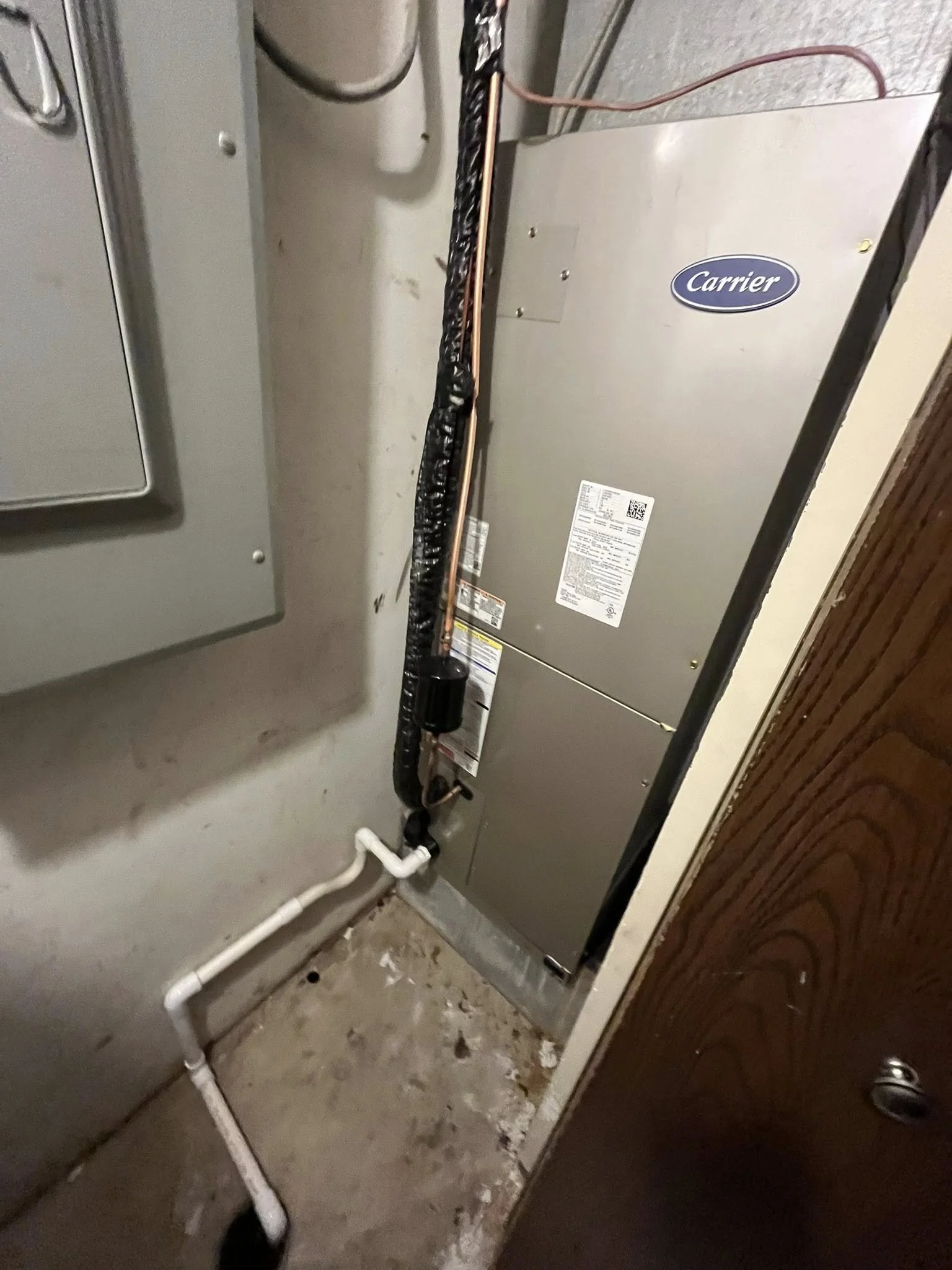 View of an HVAC system, including a Carrier air handler, pipes, and electrical components in a utility closet.