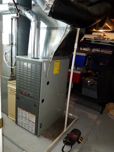 An HVAC furnace unit with ducts and insulated piping in a basement mechanical room.