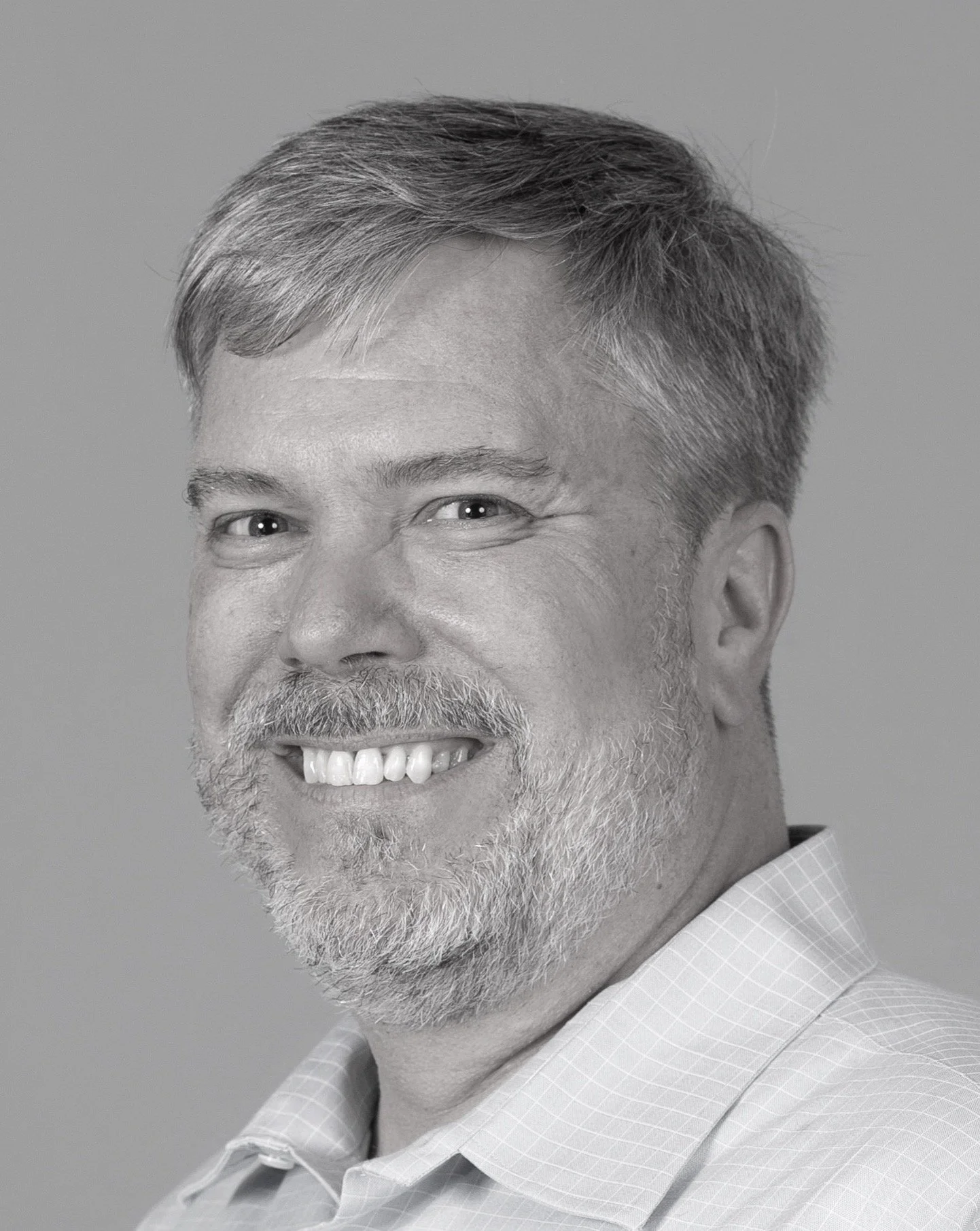 Black and white headshot of a middle-aged man with short, pointy hair, a beard, and a smile, wearing a collared shirt.