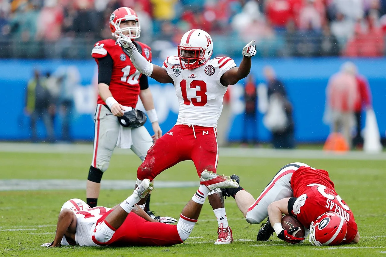American football players in red and white uniforms on the field during a game, with one player standing and celebrating while others are on the ground.