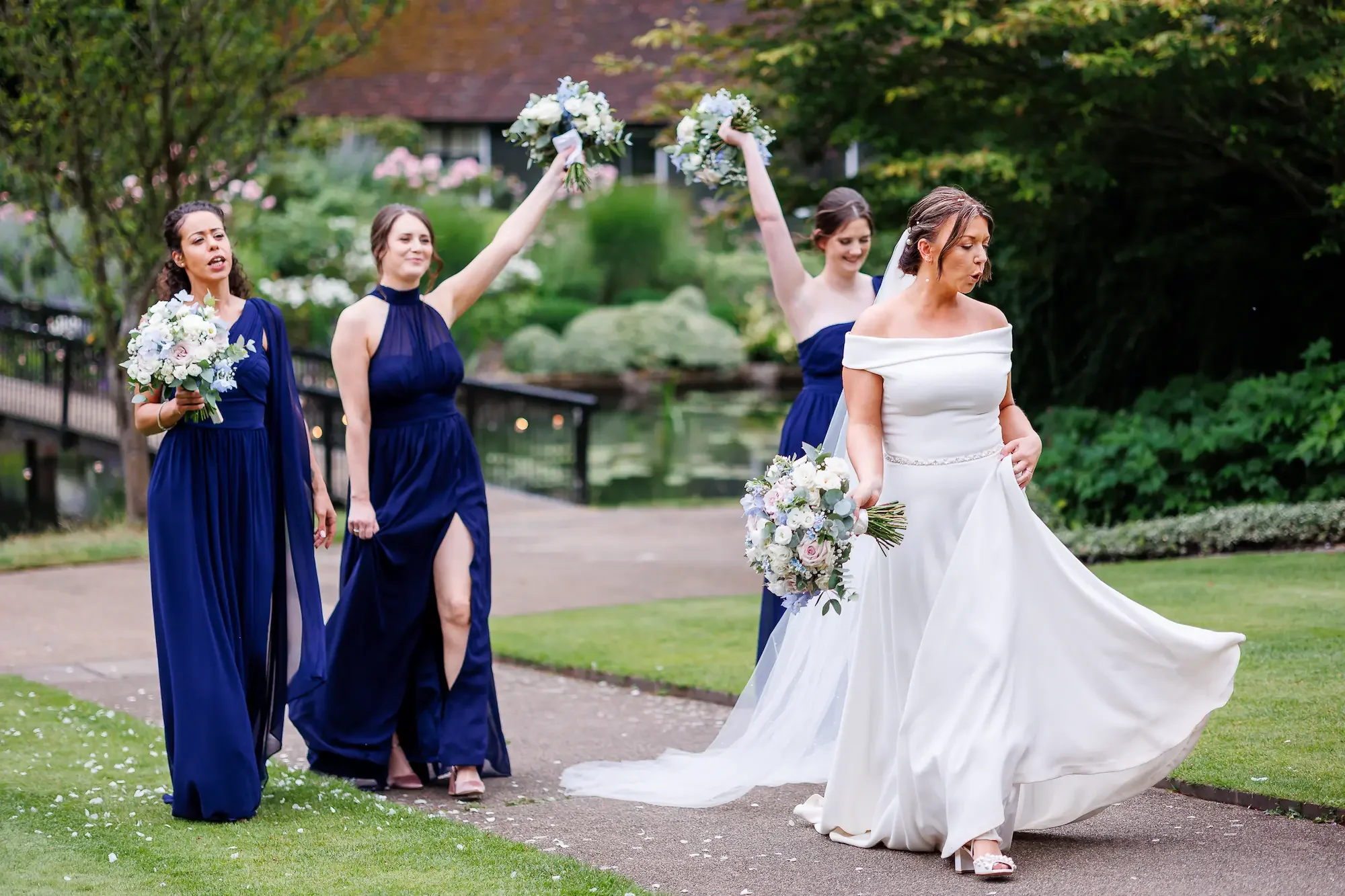 Bride strutting with bouquet in one hand as bridesmaids in royal blue dresses strut behind at The Orangery in Maidstone.