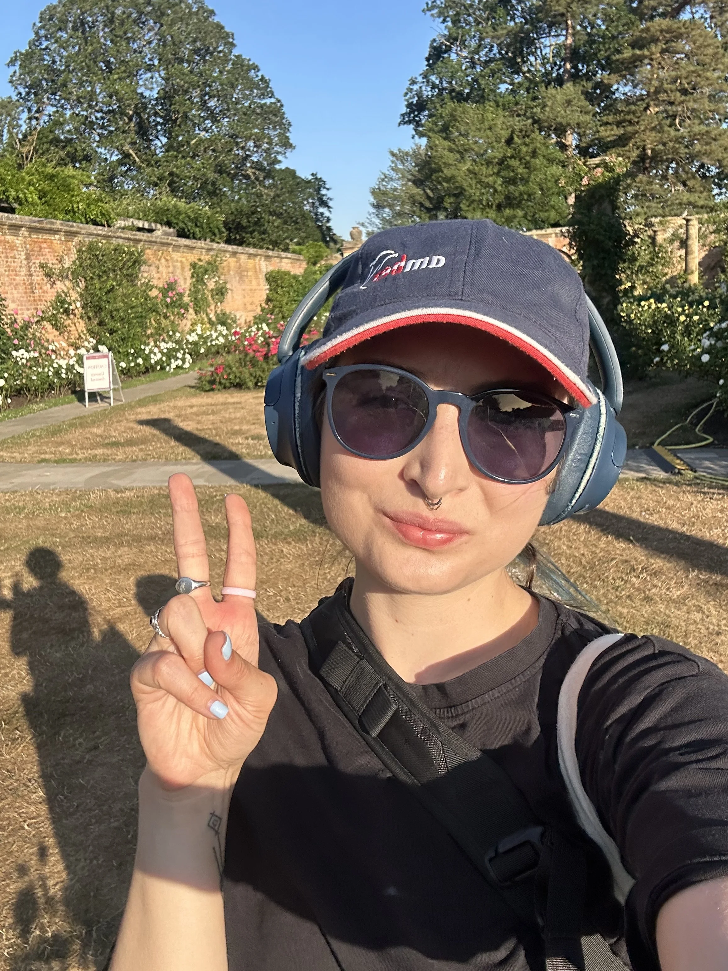Nastia in a baseball cap, sunglasses and big headphones taking a selfie in the rose garden at Hever Castle