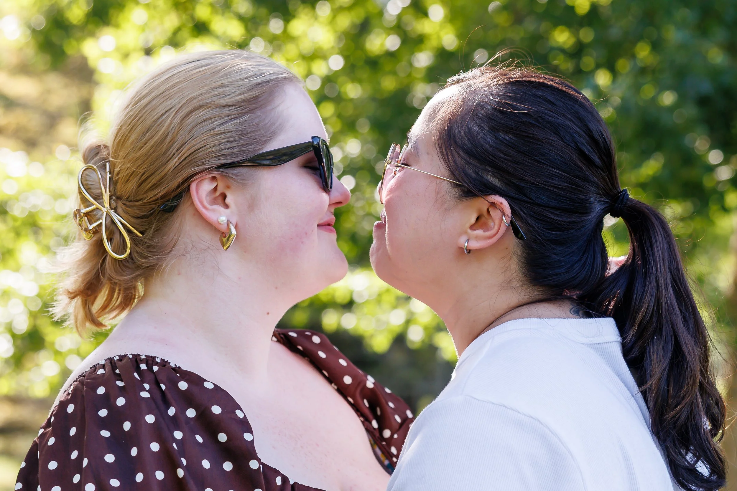 Queer sapphic couple grinning at each other moments before a kiss.