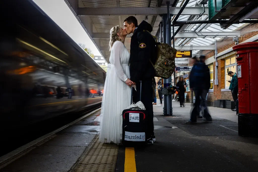Newlywed couple kissing and holding a suitcase saying Just Married as a train comes into Dover Priory station with motion blurred. This is a Kent micro wedding by Nastia Photography.