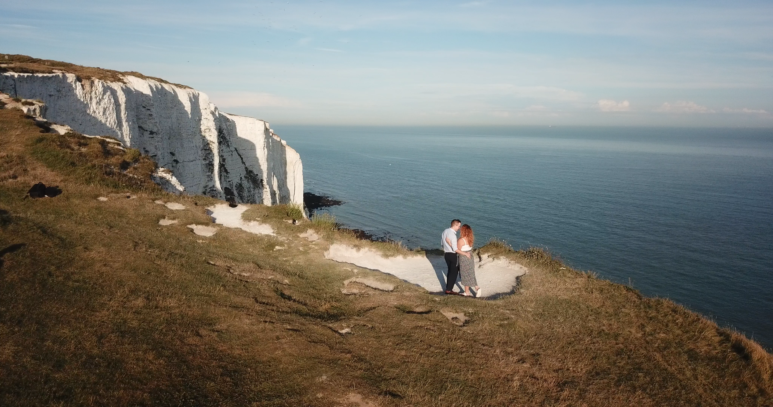 Drone photo of the couple after their secret proposal moment. You can see the white cliffs and sea.