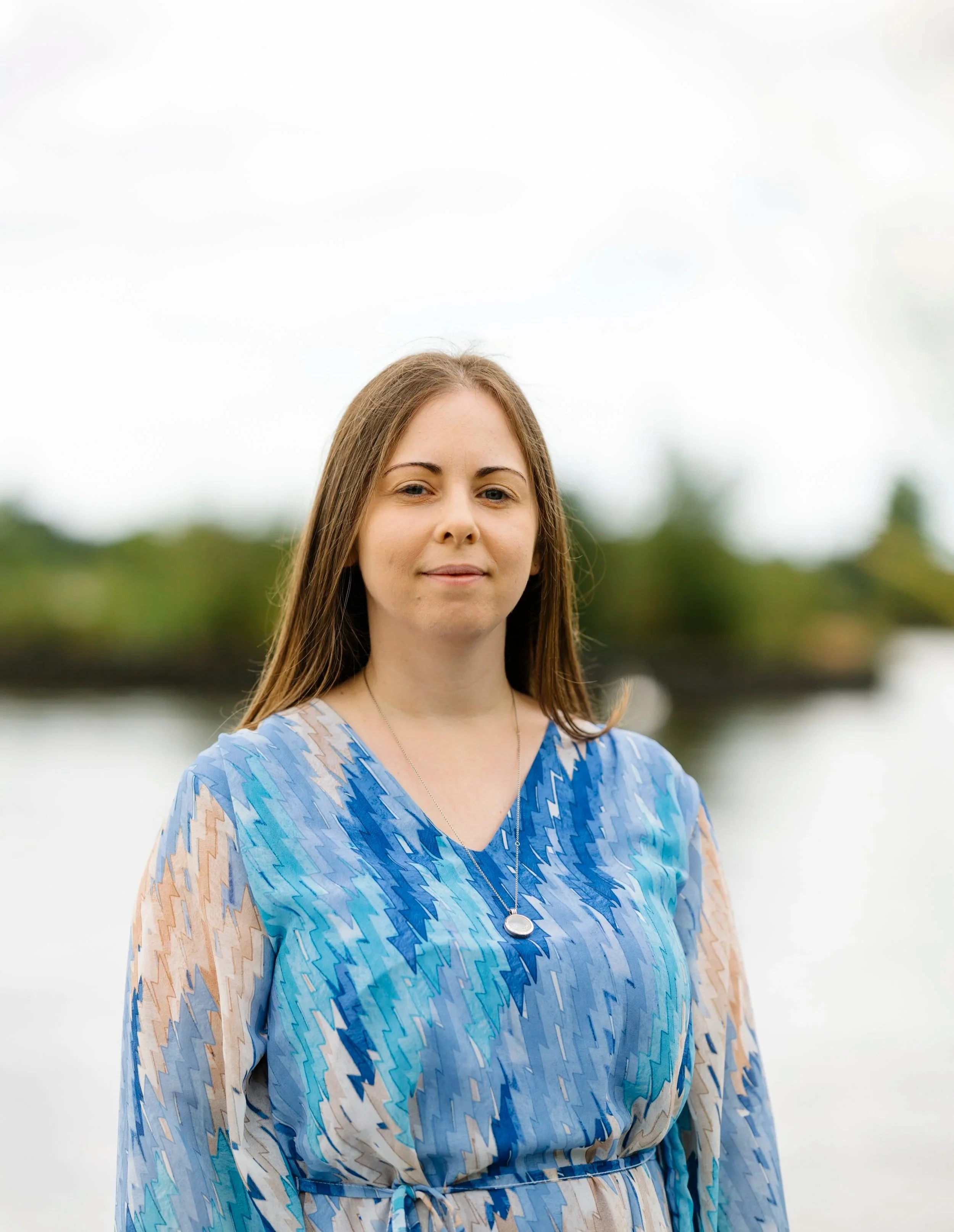 Laurie Hole, UK-based online counsellor, smiling in a relaxed portrait photograph in front of a Poole Park lake.