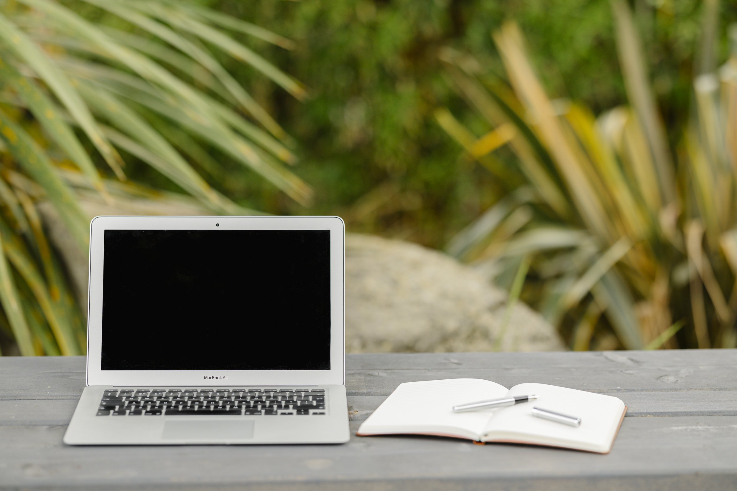 Laptop, notebook and pen on a bench outdoors, representing a calm space for reflection
