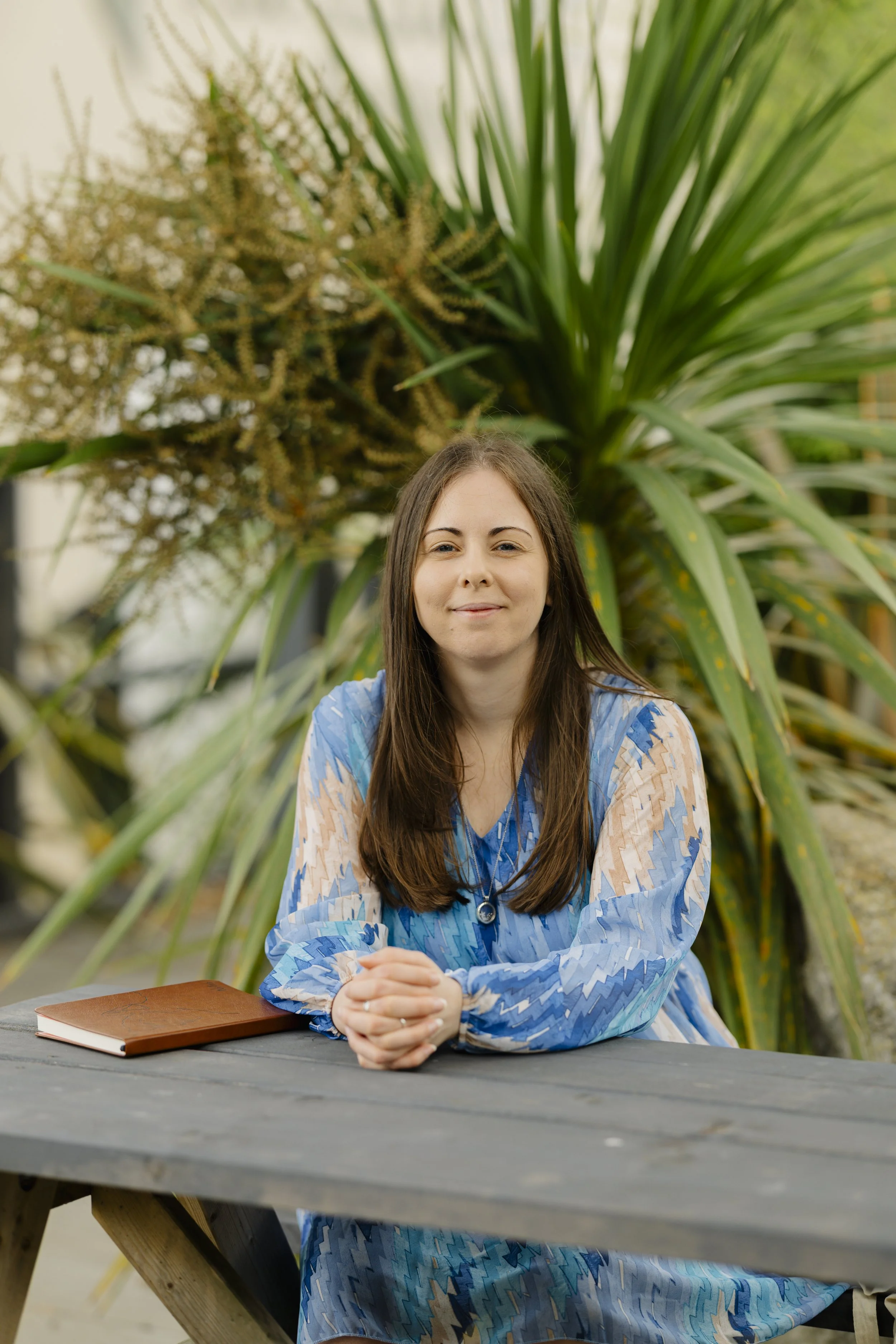 Laurie Hole, UK-based online counsellor, sitting and smiling at the camera with a notebook beside her.