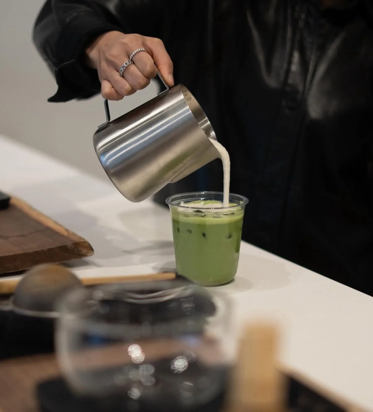 Person pouring milk into a cup of iced matcha green tea.