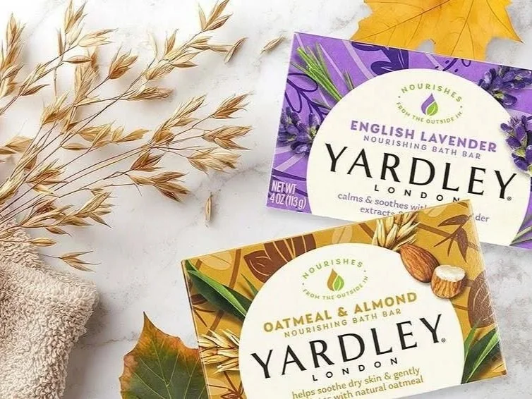 Two Yardley London bath bars, one English Lavender and one Oatmeal & Almond, placed on a white marble surface with dried wheat, a yellow maple leaf, and a purple flower in the background.
