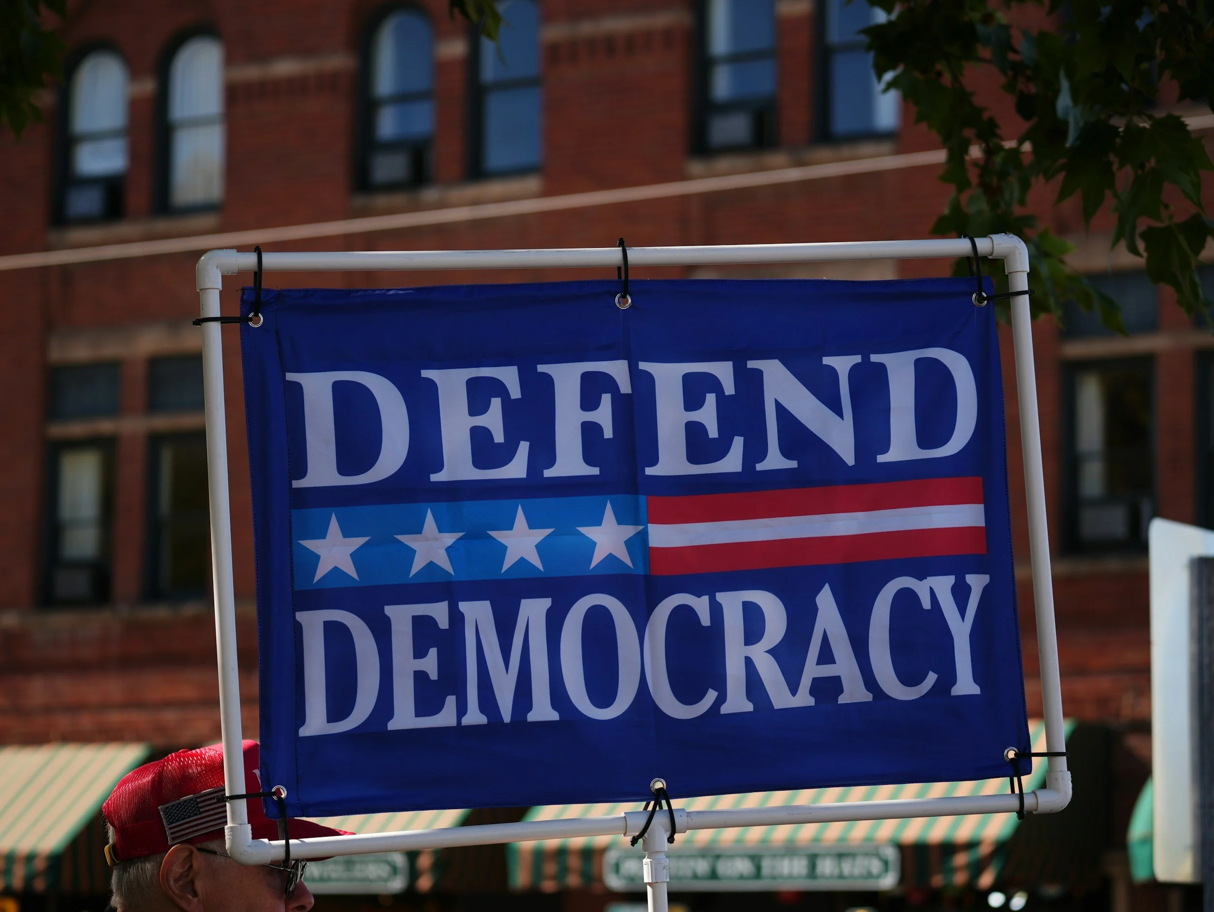 Sign with the words 'Defend Democracy' against a city street backdrop.