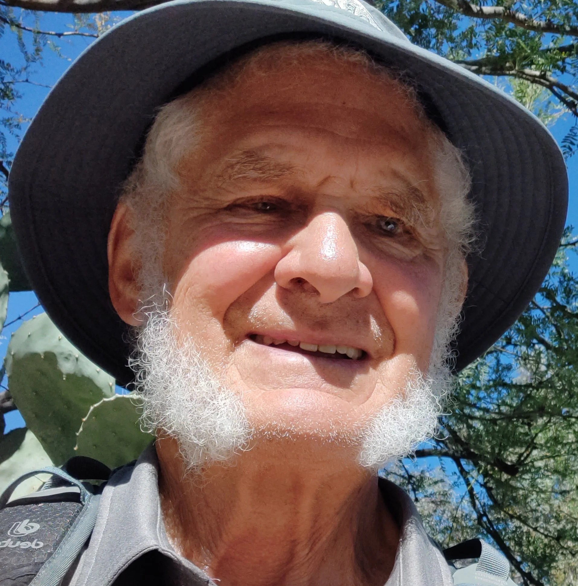 Close-up of an elderly man with white beard wearing a wide-brimmed hat outdoors on a sunny day.