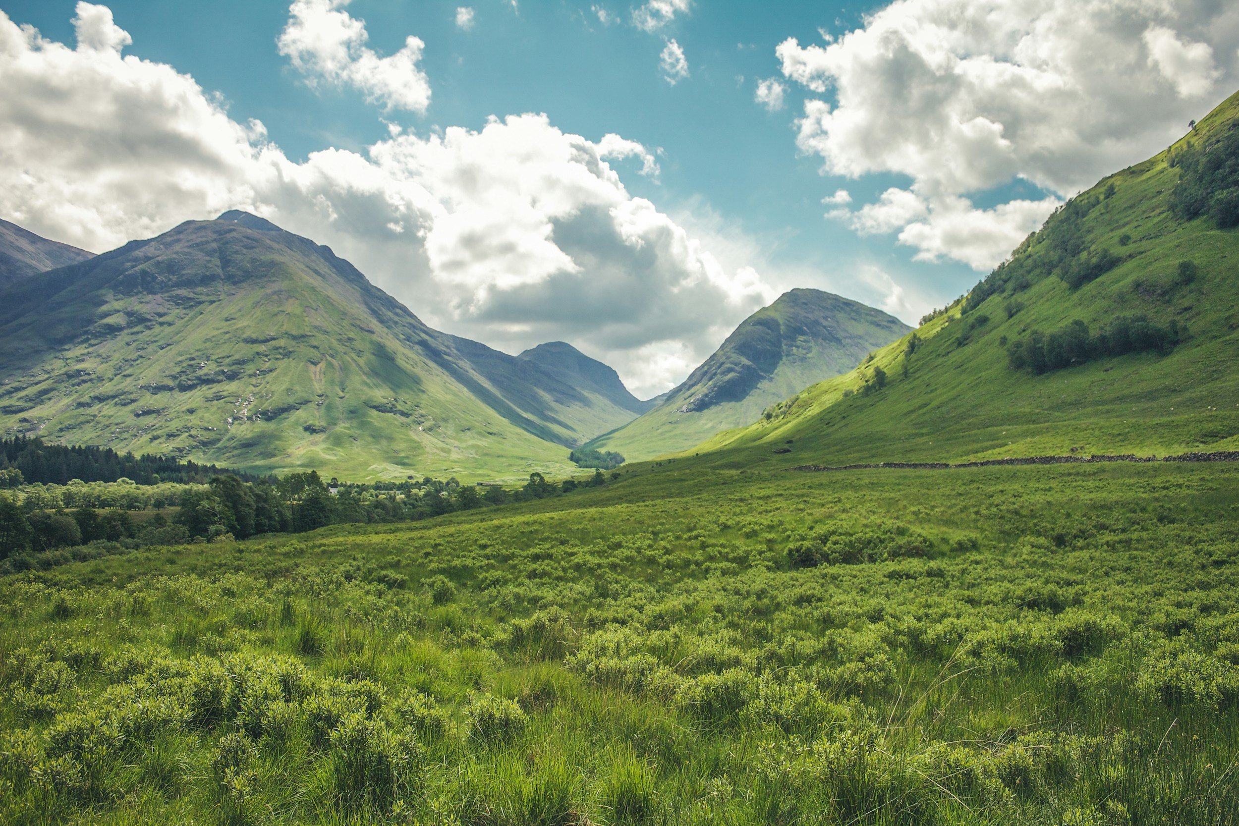 Green valley with rolling hills and mountains under a partly cloudy sky.