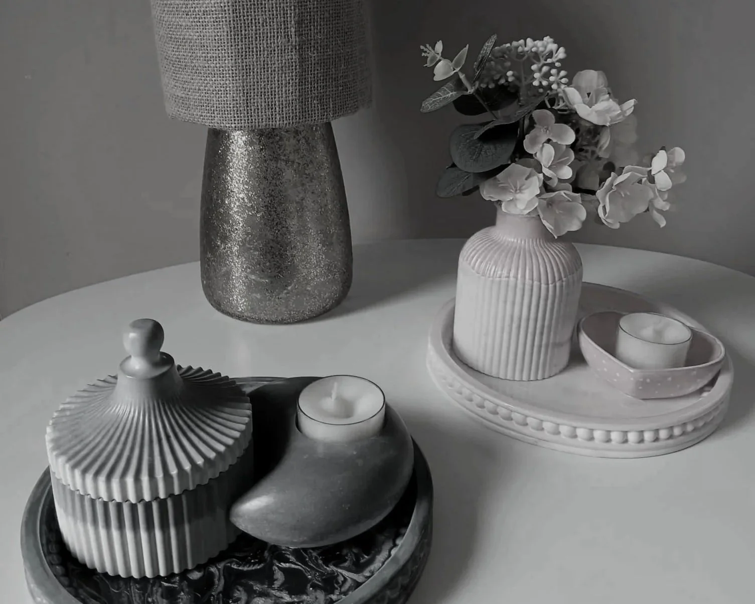 Black and white photo of Irish handmade decorative vases, candles, and tray on a round table, with a flower arrangement in the background.