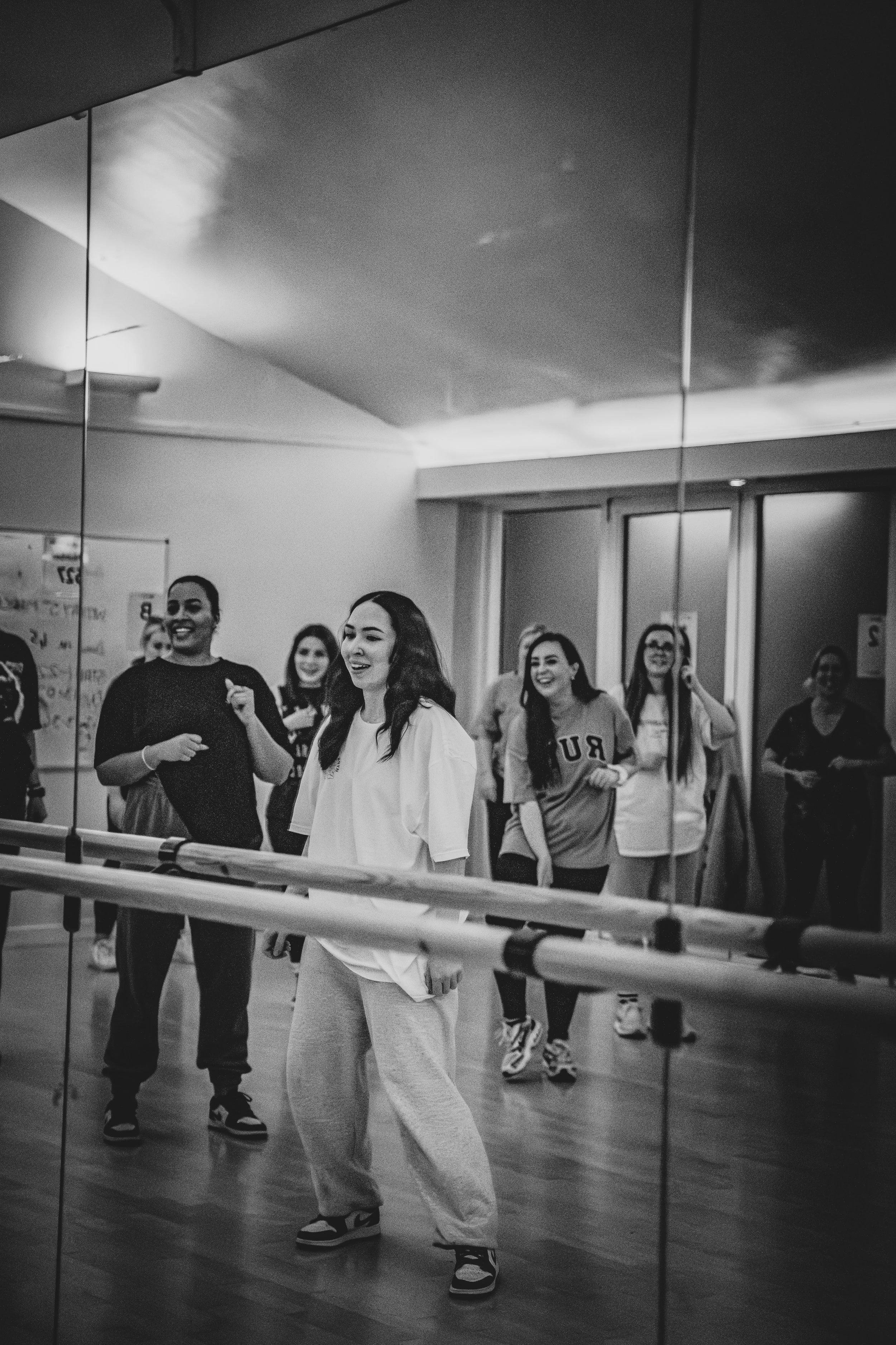 Group of women dancing and smiling in a dance studio with a large mirror.