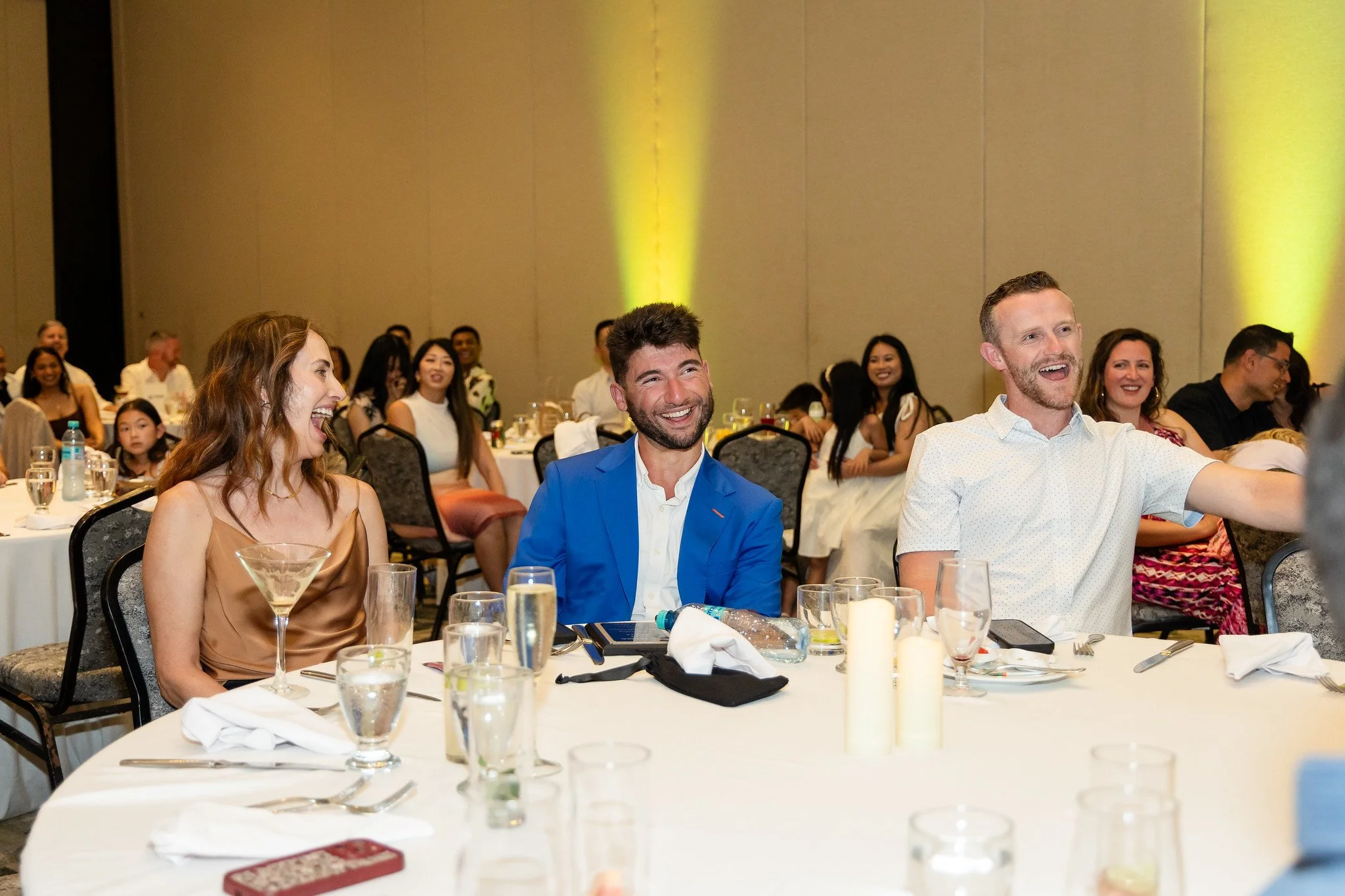 People sitting at a banquet table, smiling and laughing during a social event or celebration.