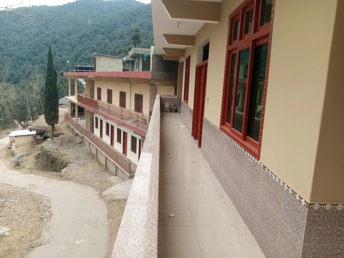 View of a building with a balcony overlooking a rural landscape with trees and hills, in a mountainous area.