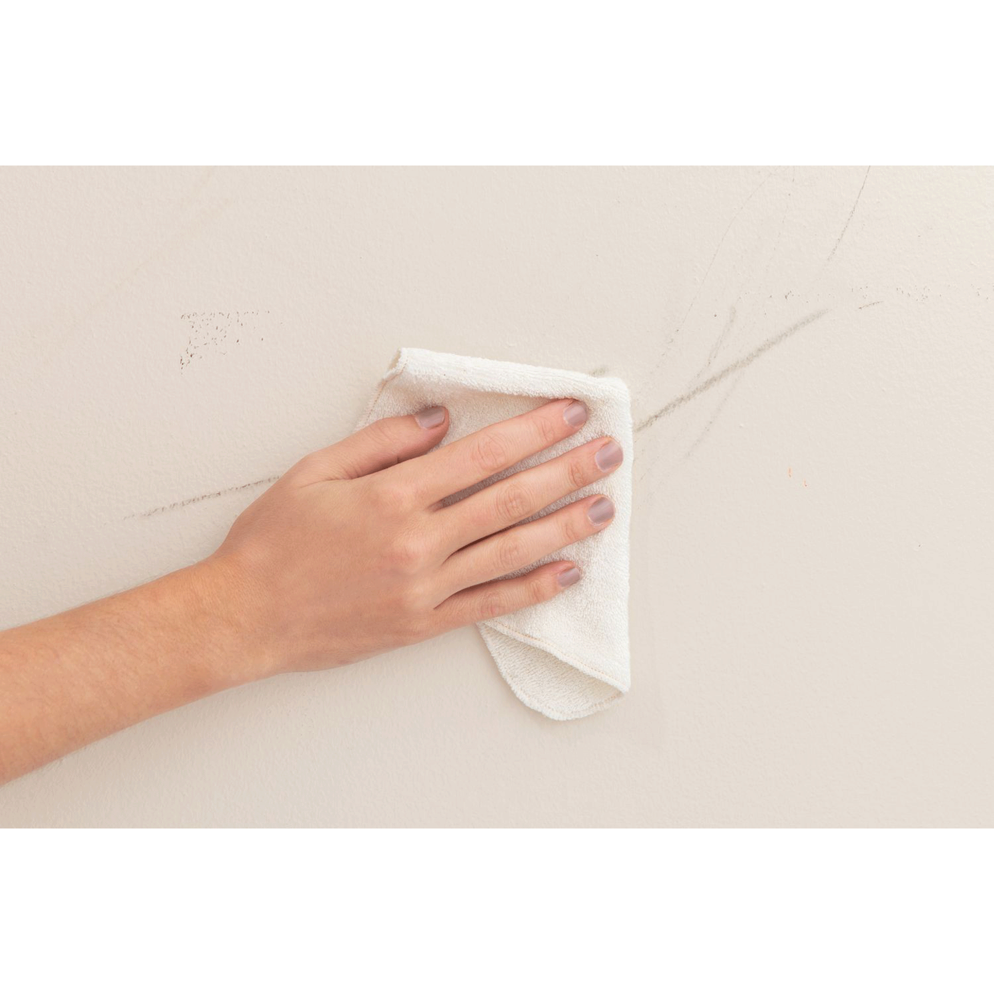 Hand wiping a crack on a white wall with a cloth.