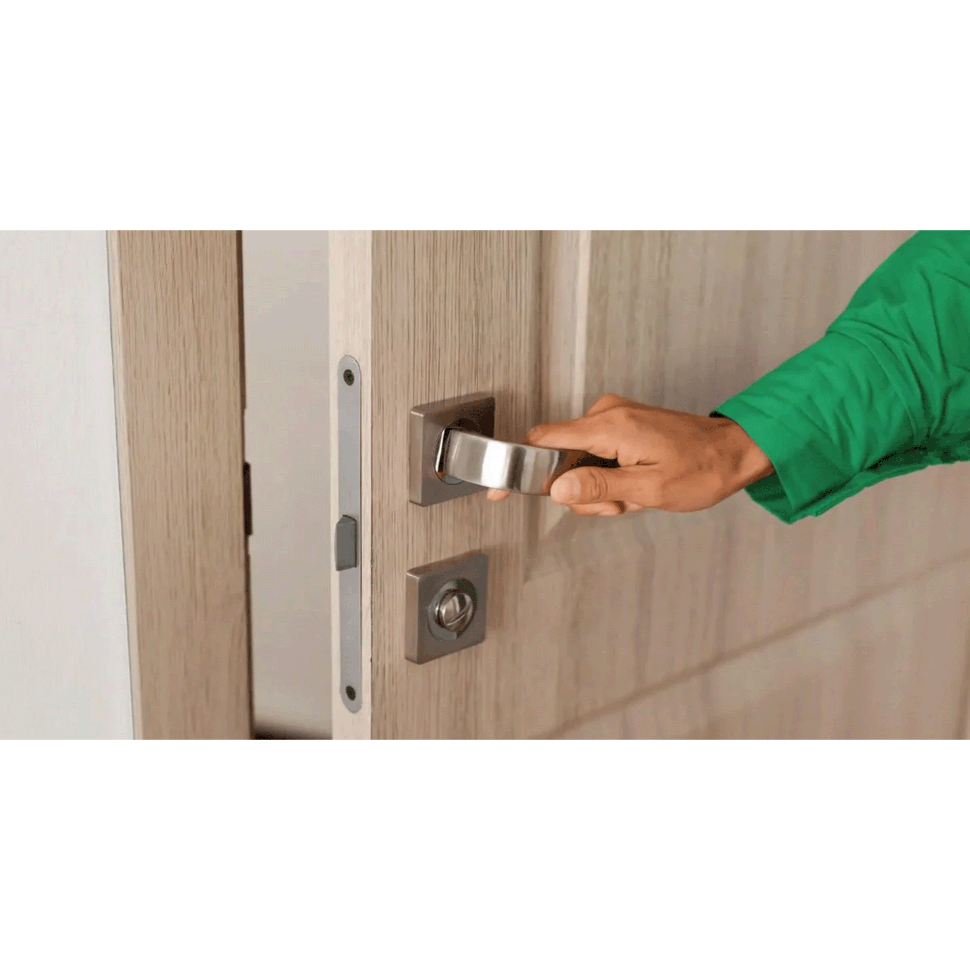 Person in green jacket opening a wooden door with a metal door handle and lock.
