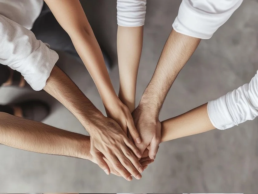 Cinque persone che pongono le mani una sopra l'altra, simboleggiando collaborazione e unità.