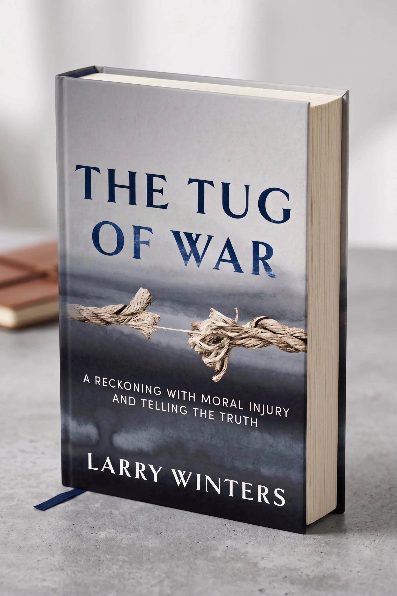 Close-up of a book titled 'The Tug of War' by Larry Winters, with a picture of a tangled, frayed rope on the cover, set on a light grey surface.