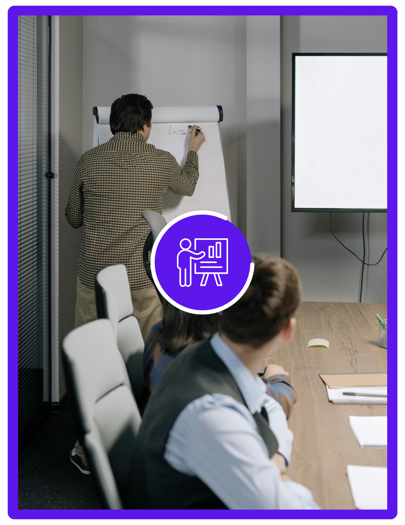 A man is writing on a whiteboard in a conference room with three seated people watching.