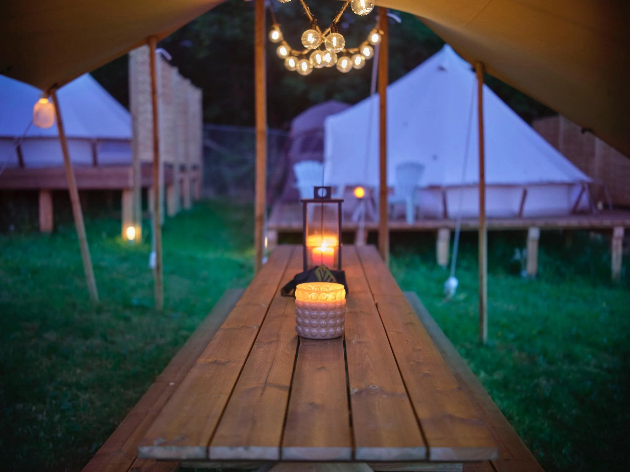 Une tente installée dans un jardin avec des éclairages à l'intérieur, une table en bois avec des bougies allumées