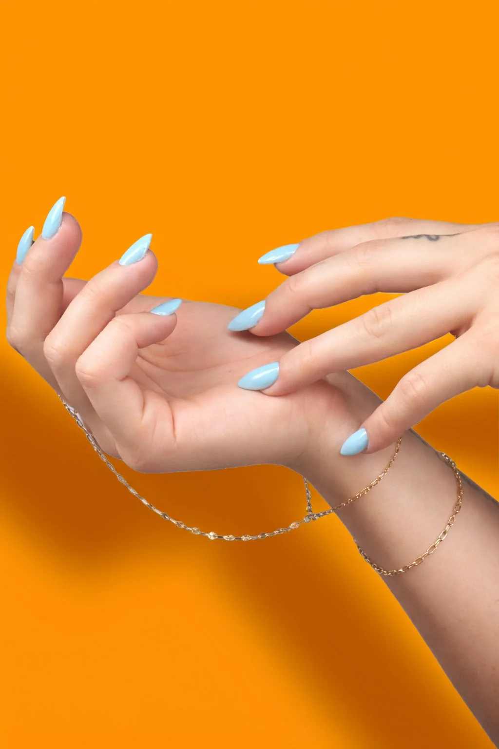Close-up of two hands with light blue manicured nails, jewelry, and a tattoo with an orange background.